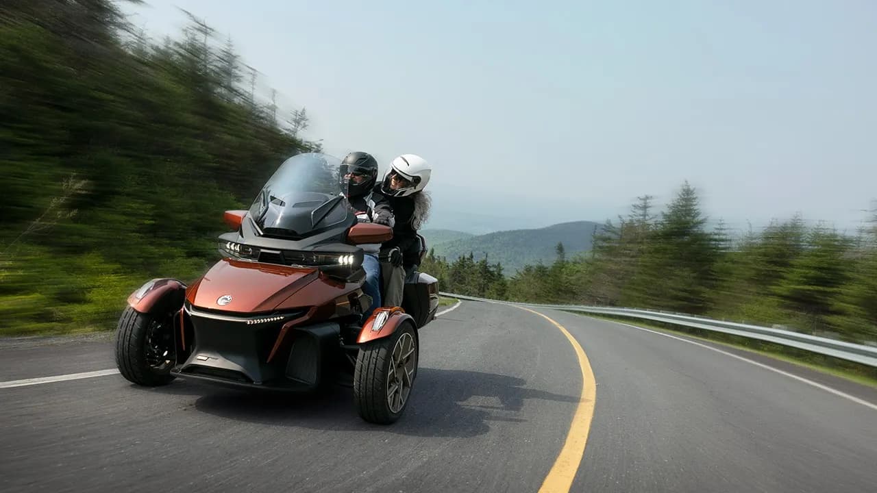 Can-Am Spyder RT с водителем и пассажиром на извилистой асфальтовой дороге.