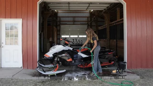 Женщина моет Ski-Doo Summit из садового шланга перед гаражом