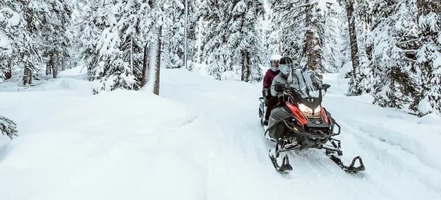 Два человека едут на Ski-Doo Expedition по заснеженному лесному маршруту