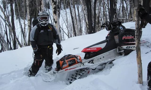 Райдер рядом со снегоходом Polaris RMK, застрявшим в глубоком снегу