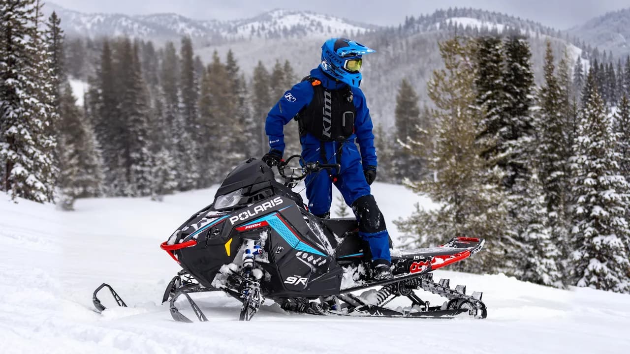 Райдер стоит на Polaris RMK Factory Edition 2027 в заснеженных горах
