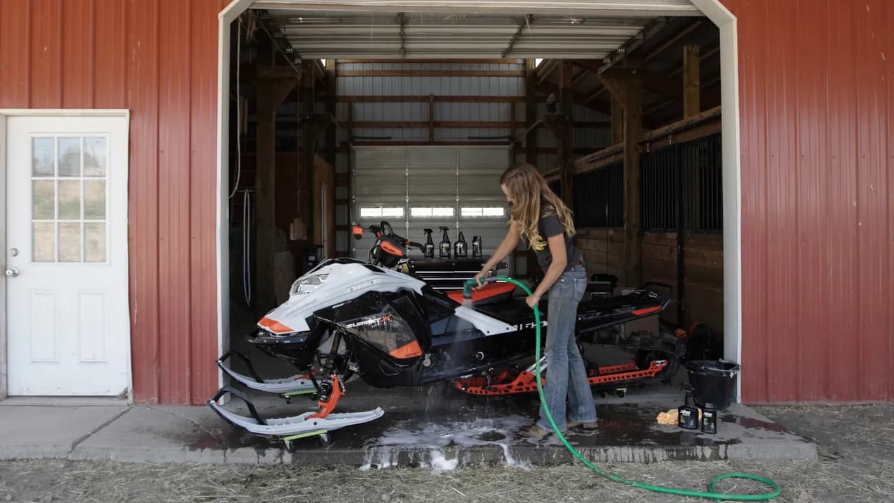Женщина моет Ski-Doo Summit из садового шланга перед гаражом