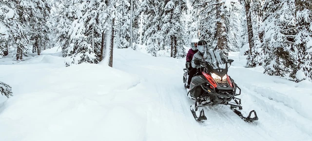 Два человека едут на Ski-Doo Expedition по заснеженному лесному маршруту