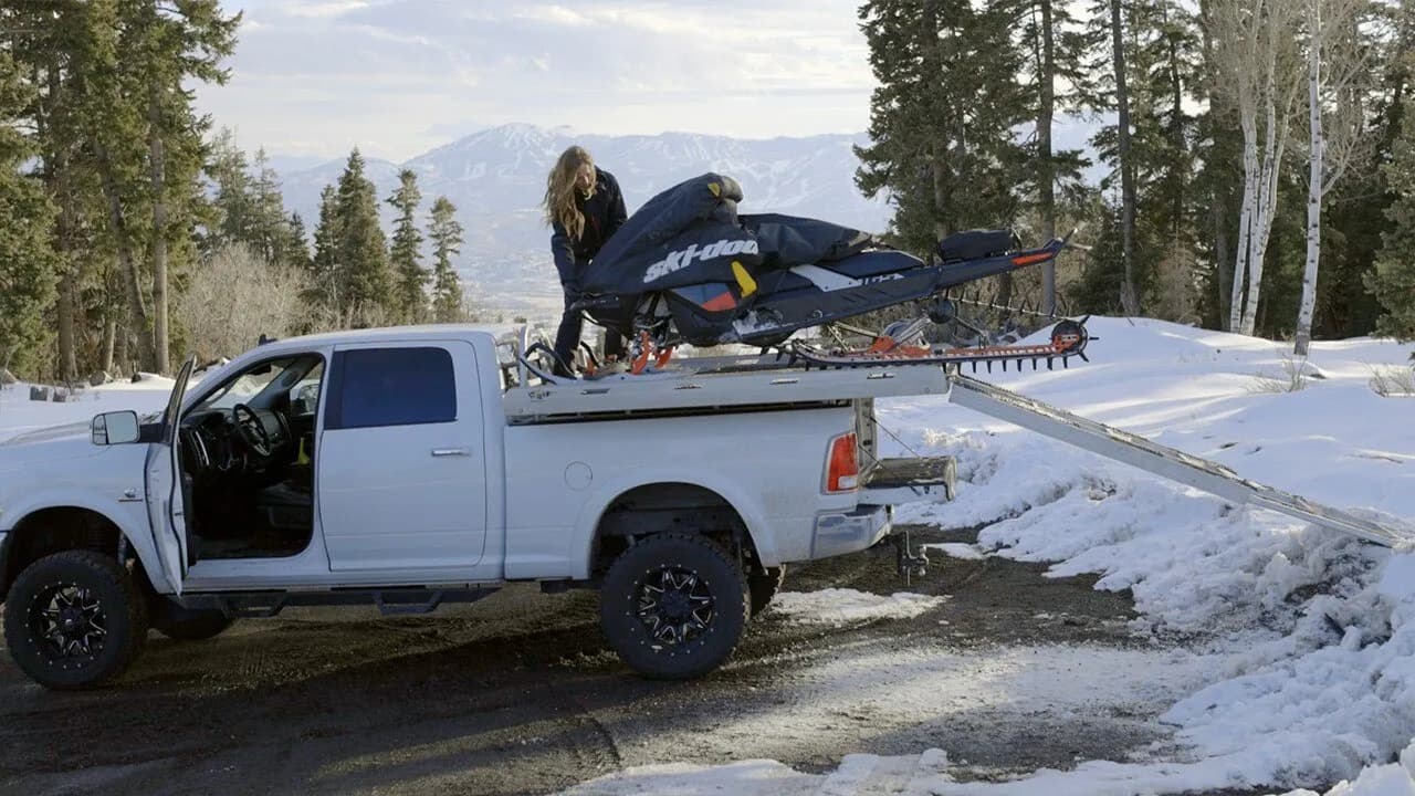 Женщина надевает чехол на Ski-Doo на платформе над кузовом пикапа