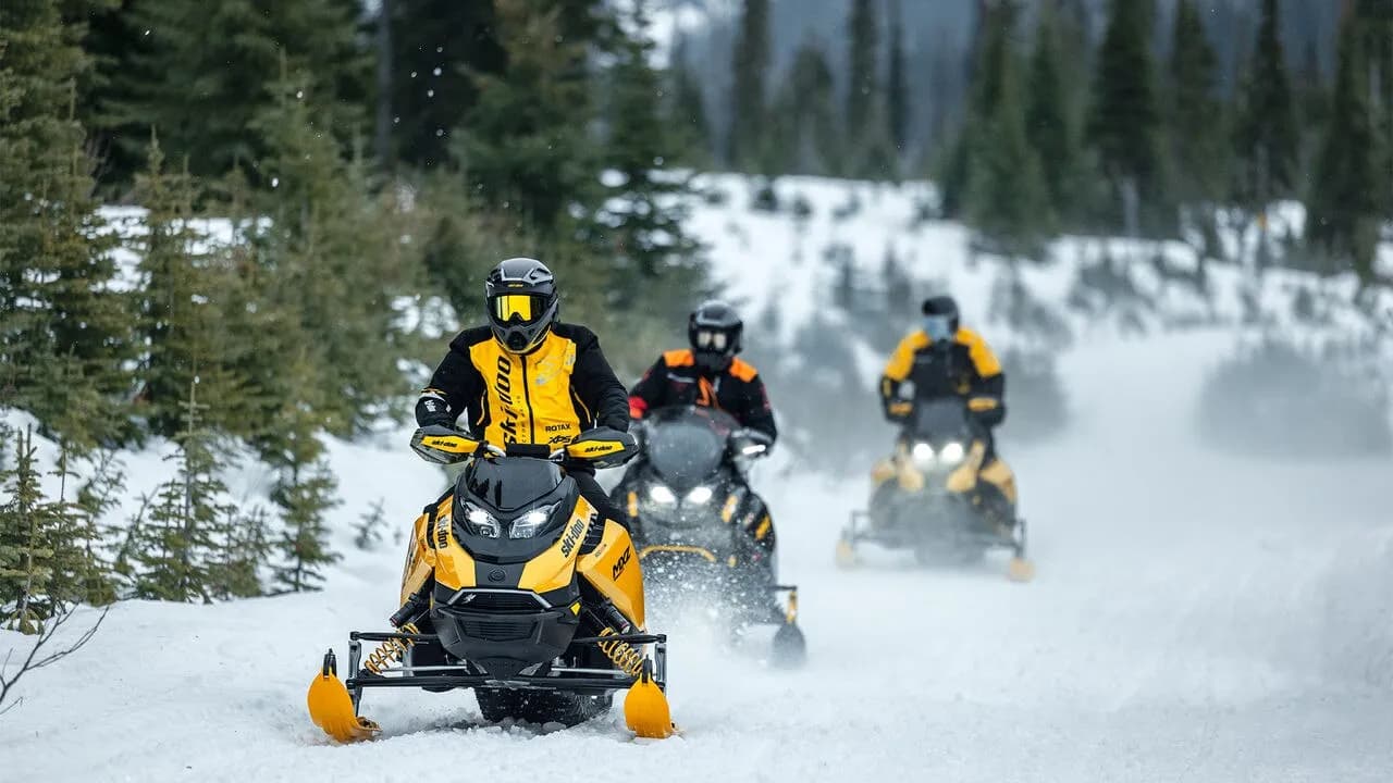 Три водителя на снегоходах Ski-Doo едут по заснеженной лесной трассе