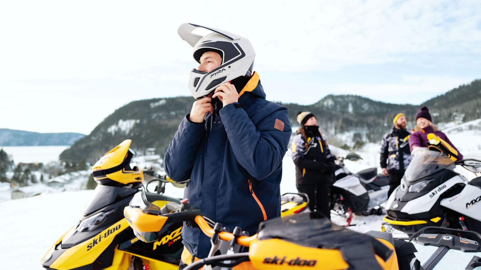 Водитель застёгивает шлем рядом со снегоходами Ski-Doo